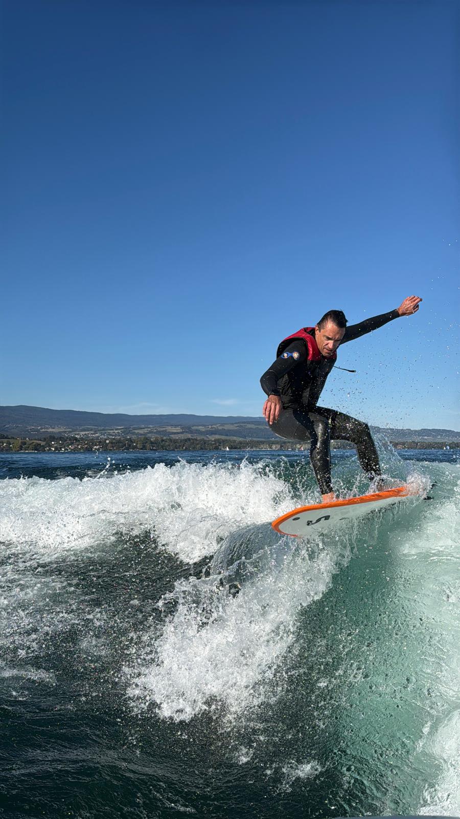 Rider en wakesurf dans la vague de l'Axis T22 sur le lac Léman, chaîne du Mont-Blanc en arrière-plan